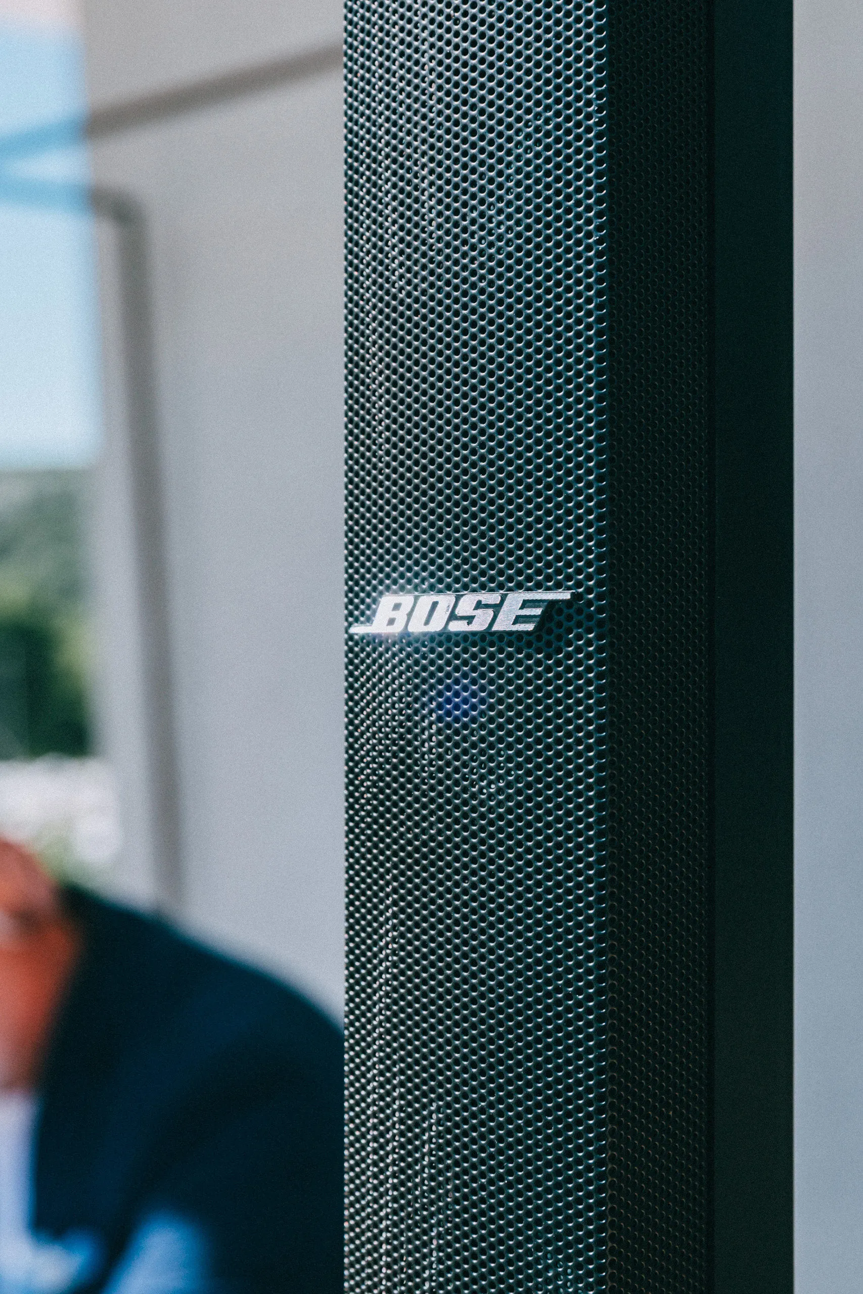Close-up of a Bose speaker with DJ performing in the background at an outdoor event