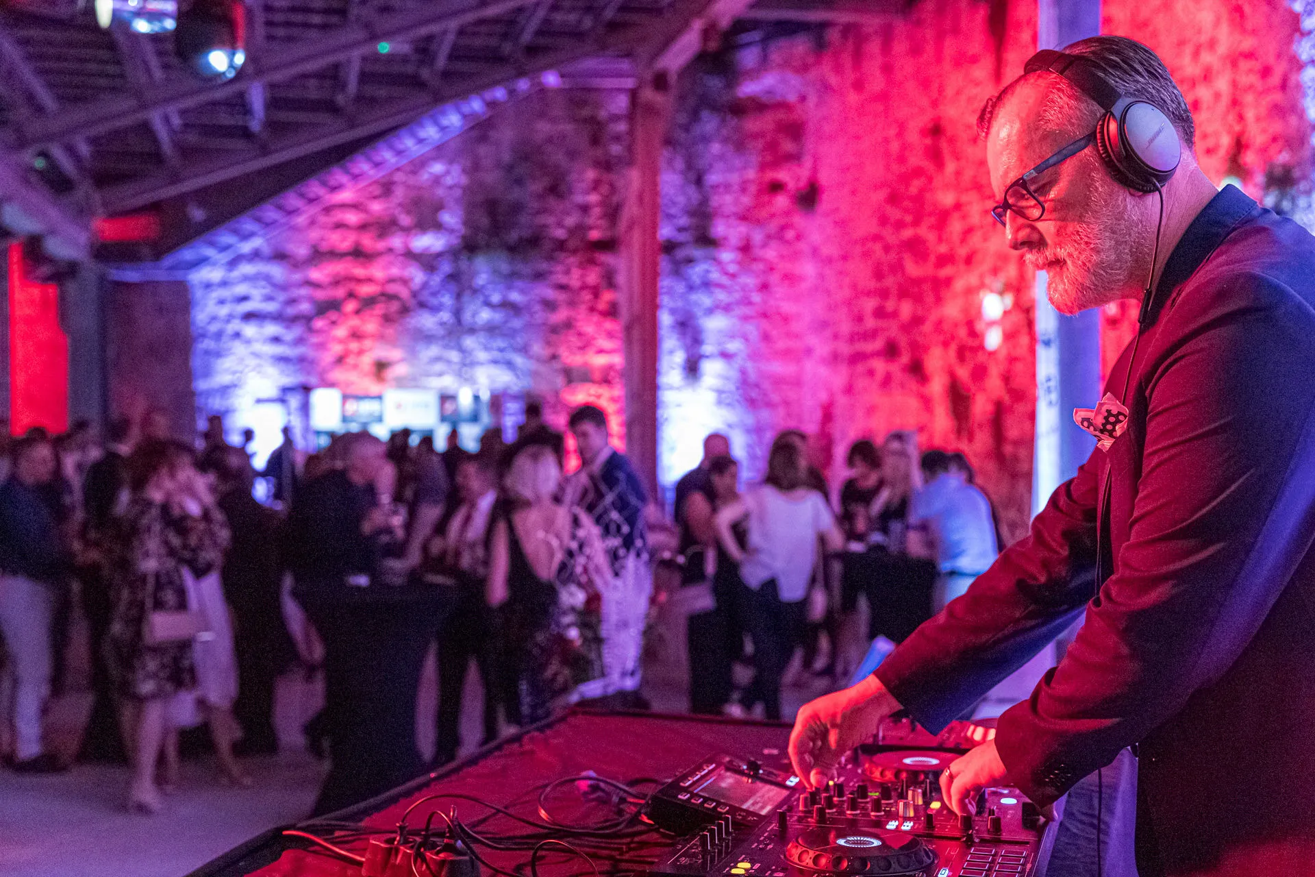 DJ performing at a gala event inside a historic stone fortress venue with dramatic purple and red uplighting — Cosmic Production