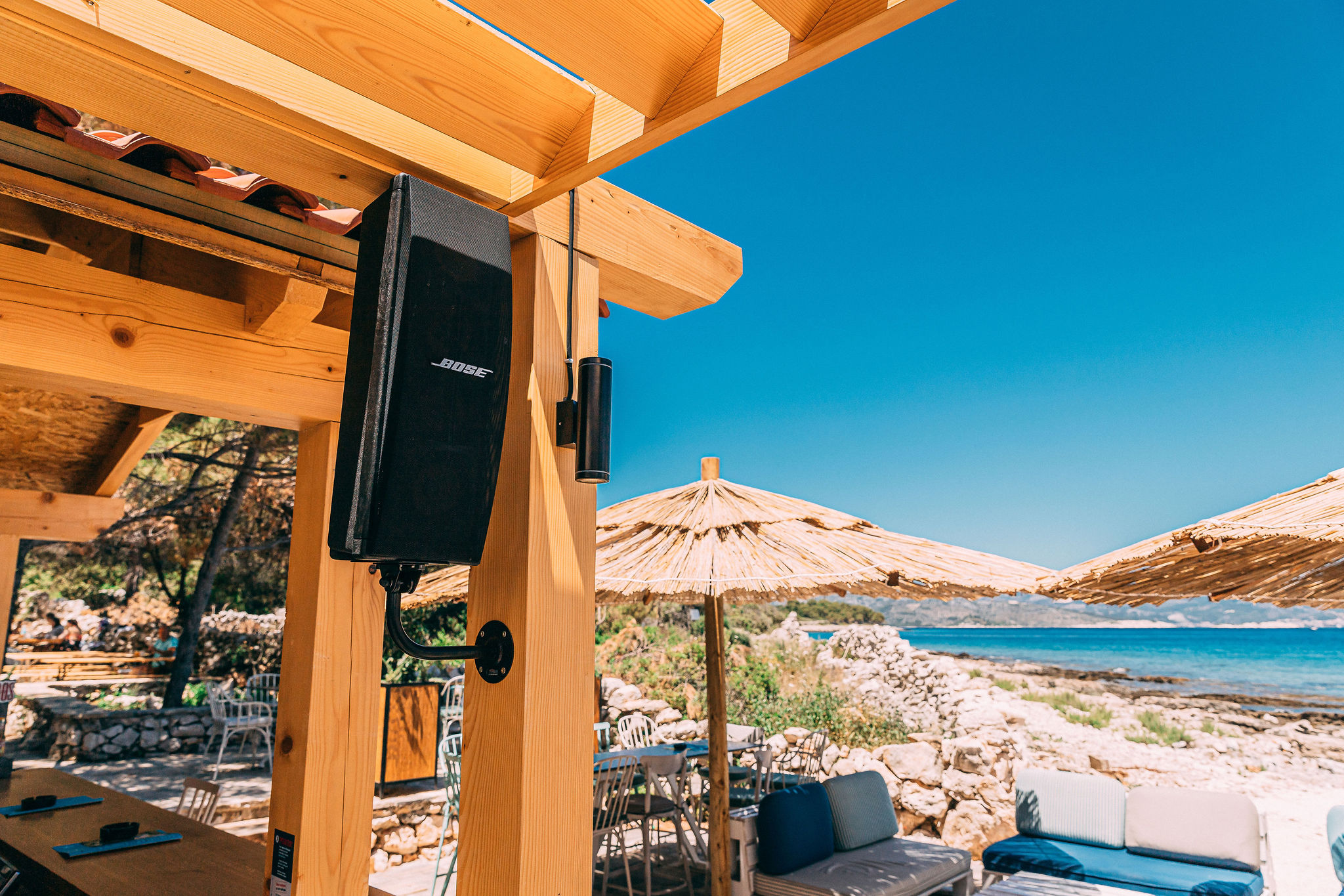Haven Beach Bar with Bose speaker on post, straw umbrellas, and Adriatic Sea view