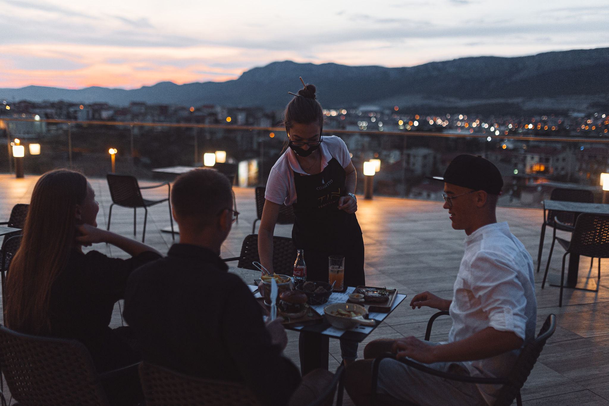 Split rooftop residency with diners, sunset, and a DJ in the background