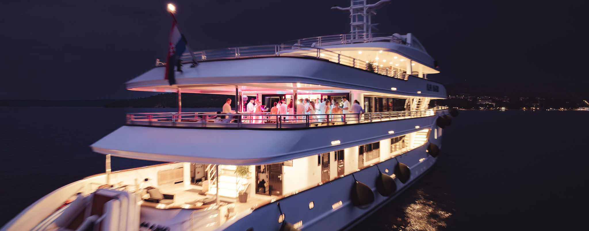 Private yacht party at night on Yacht Alfa Mario with guests on illuminated deck in the Adriatic Sea